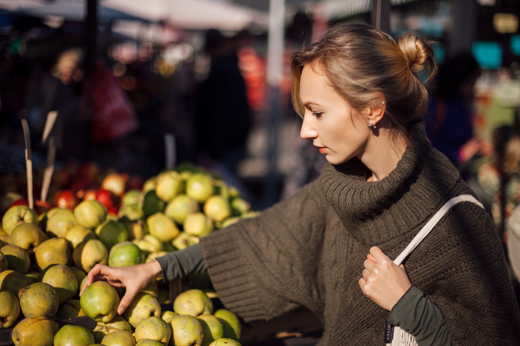 Woman examining fresh apples at a market stall.